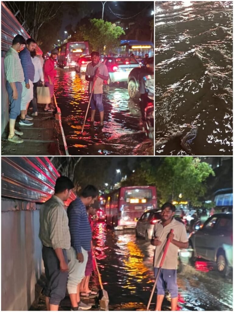 Workers clearing drainage beside vehicles on a waterlogged road at Kundalahalli Colony in Garudacharpalya
