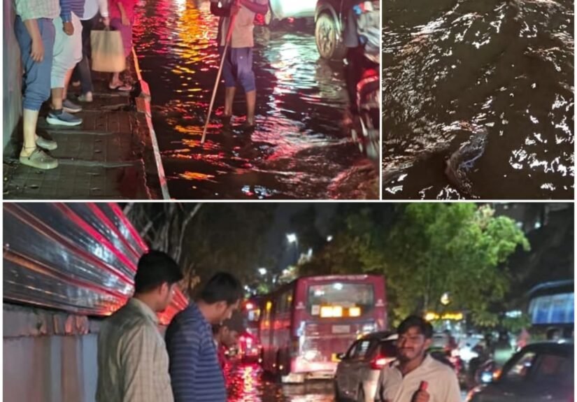 Workers clearing drainage beside vehicles on a waterlogged road at Kundalahalli Colony in Garudacharpalya