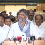 DK Shivakumar speaking to reporters at a podium with microphones