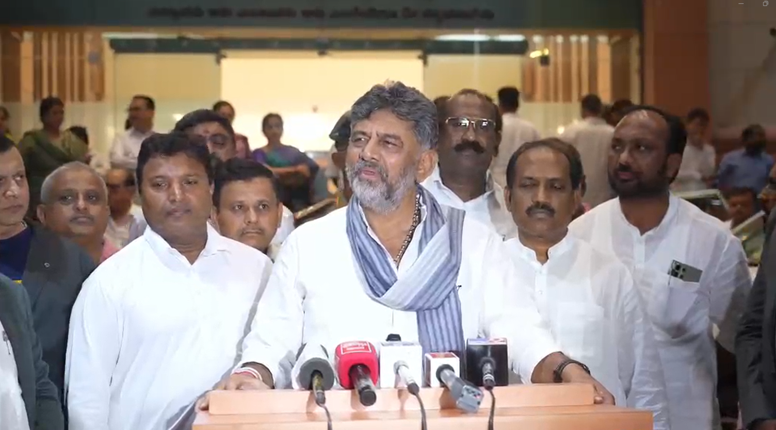 DK Shivakumar speaking to reporters at a podium with microphones