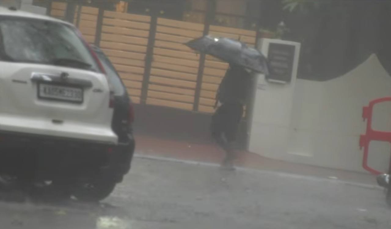 A person carrying an umbrella beside vehicles on a rain-soaked street