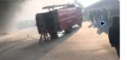 Fire engine and people near the smoke-filled industrial premises in the source video