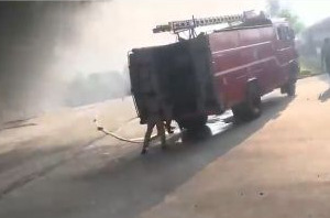 Fire engine and people near the smoke-filled industrial premises in the source video