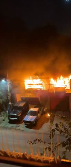 Cars parked below a garage building engulfed in flames in the source video