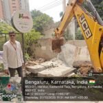 Excavator removes a compound wall during Haralur stormwater-drain encroachment clearance