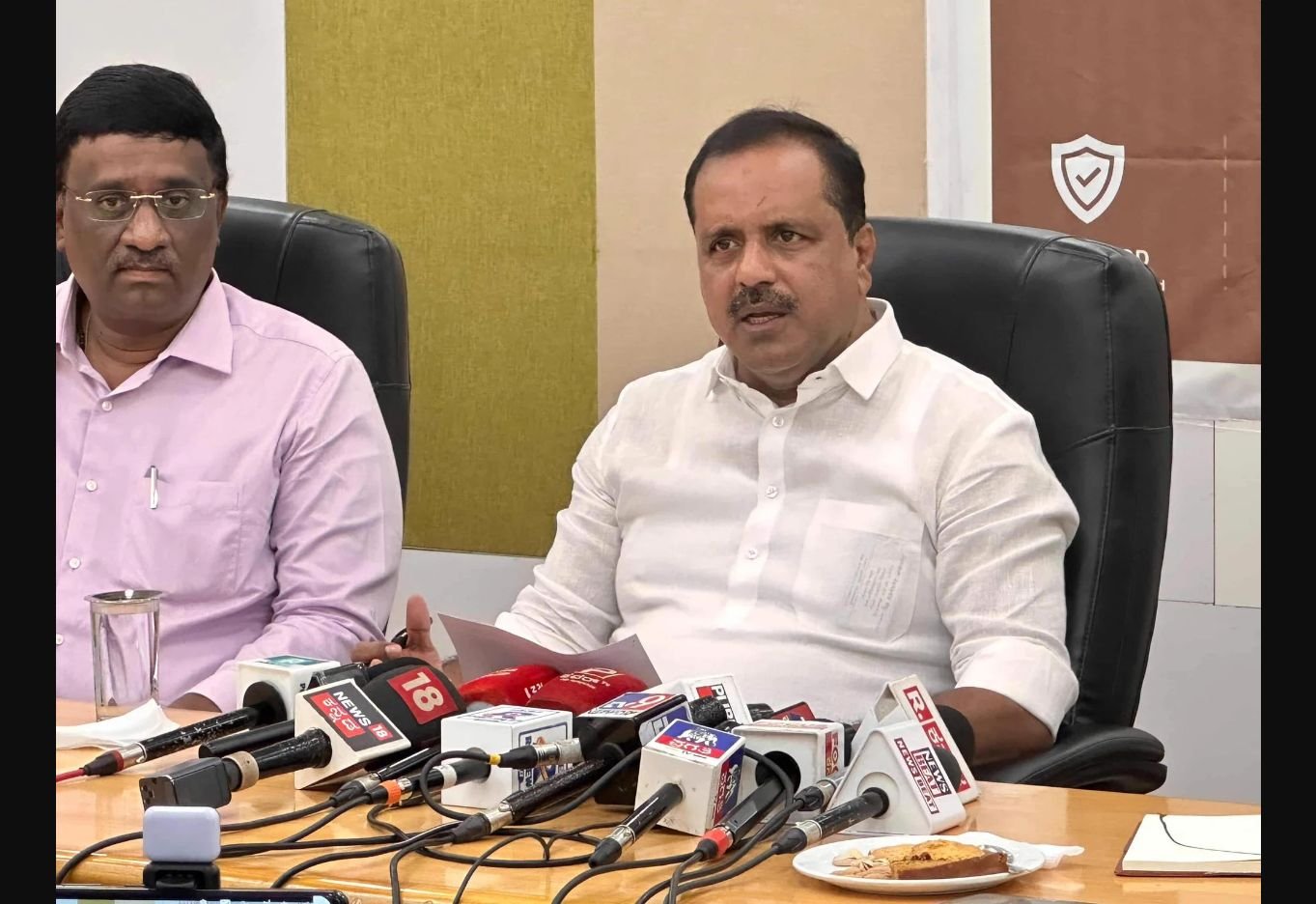 UT Khader speaking at a media briefing with microphones in front of him